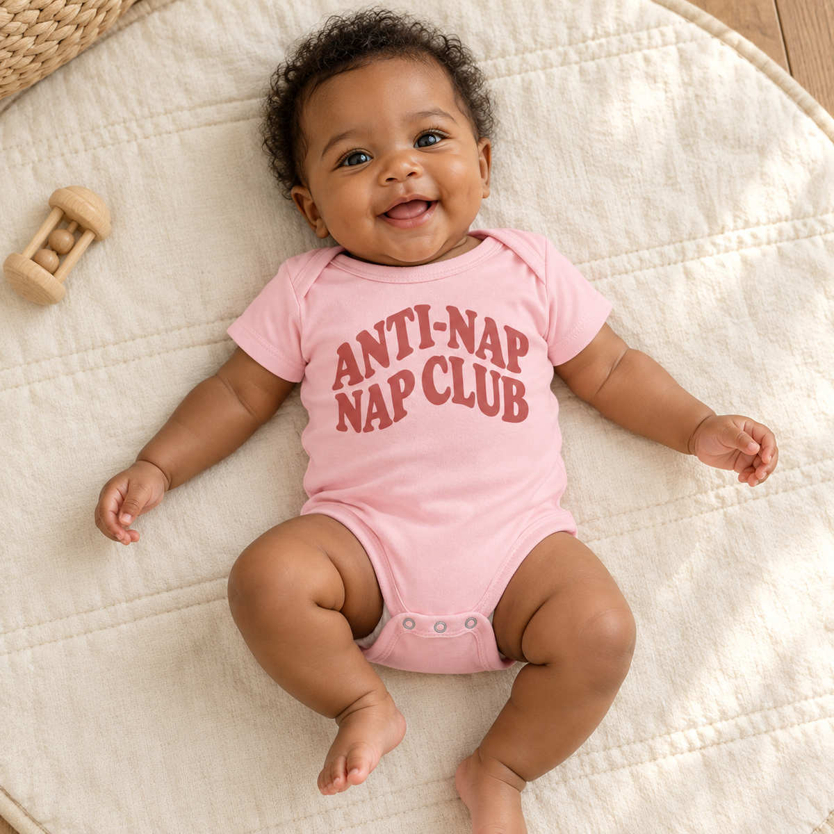 Baby wearing the Pink Anti-Nap Nap Club bodysuit on a cream play mat