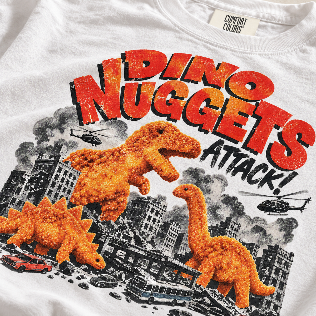 Close-up of Dino Nuggets Attack graphic on white Comfort Colors tee
